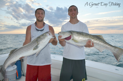 A great day fishing: two boaters pose for a photo holding large fish with ocean in background.